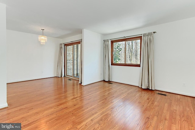 spare room with an inviting chandelier and light hardwood / wood-style floors