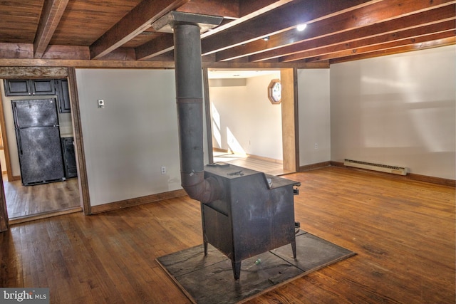 basement featuring hardwood / wood-style floors, black fridge, a wood stove, and a baseboard heating unit