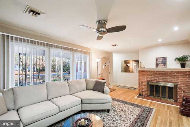 living room featuring ornamental molding, a brick fireplace, light hardwood / wood-style flooring, and ceiling fan