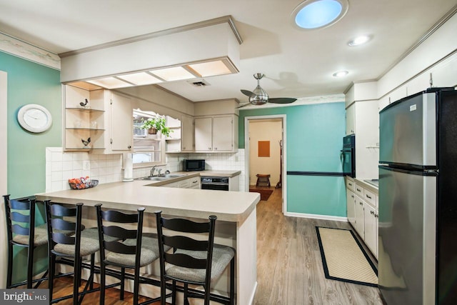 kitchen with sink, black appliances, kitchen peninsula, a breakfast bar area, and light hardwood / wood-style flooring