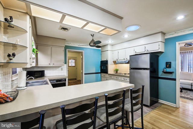 kitchen featuring black appliances, kitchen peninsula, ceiling fan, backsplash, and light wood-type flooring