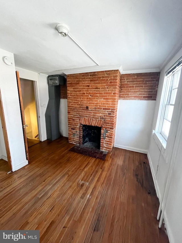 unfurnished living room with dark hardwood / wood-style floors, a brick fireplace, ornamental molding, and brick wall