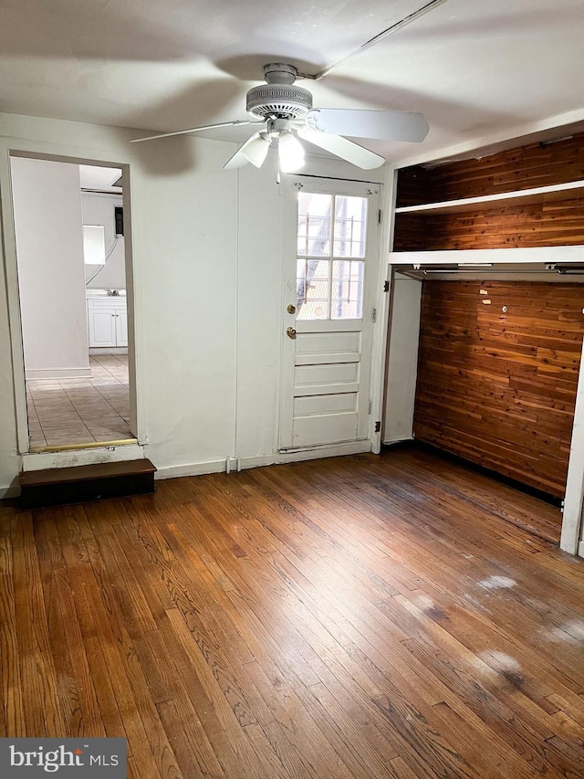 interior space featuring hardwood / wood-style floors, ceiling fan, and wood walls