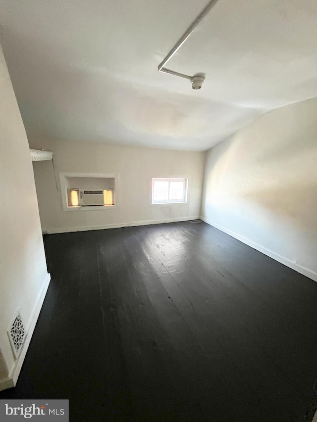 empty room featuring a wall unit AC and dark hardwood / wood-style flooring