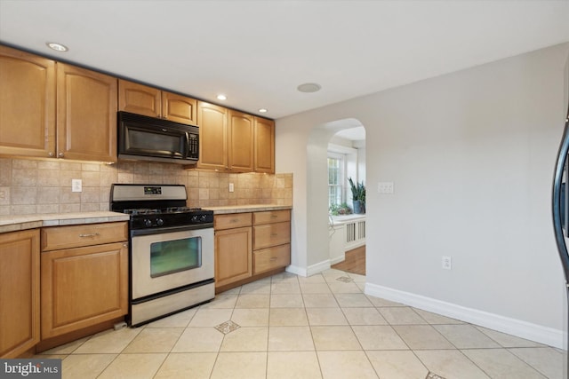 kitchen featuring fridge, tasteful backsplash, light tile patterned floors, and gas range gas stove