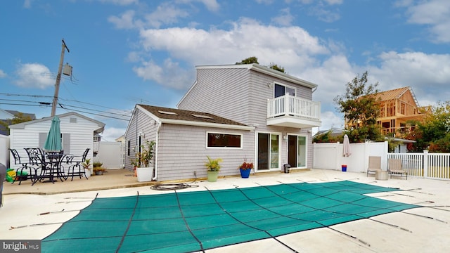 rear view of property featuring a patio, a covered pool, and a balcony