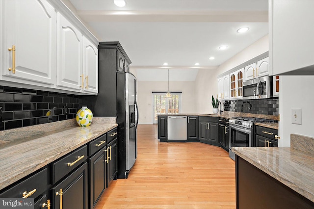 kitchen with light stone countertops, backsplash, appliances with stainless steel finishes, white cabinets, and light wood-type flooring