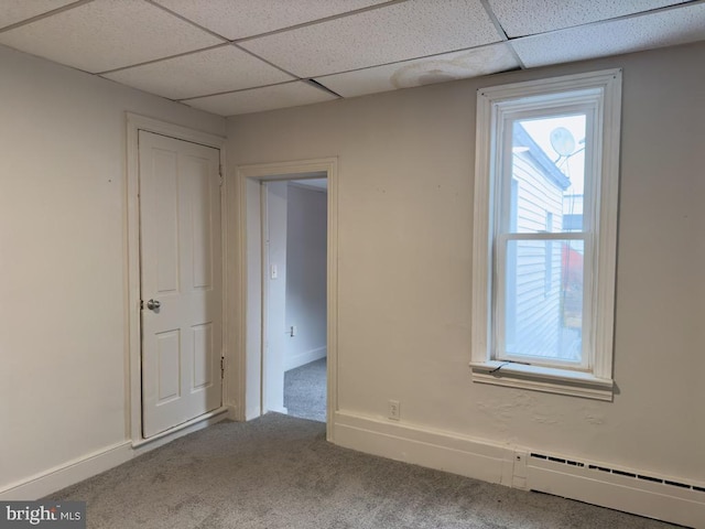 carpeted empty room with a paneled ceiling, a wealth of natural light, and a baseboard radiator