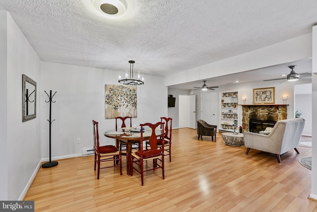 dining room with a textured ceiling, light hardwood / wood-style floors, and a stone fireplace