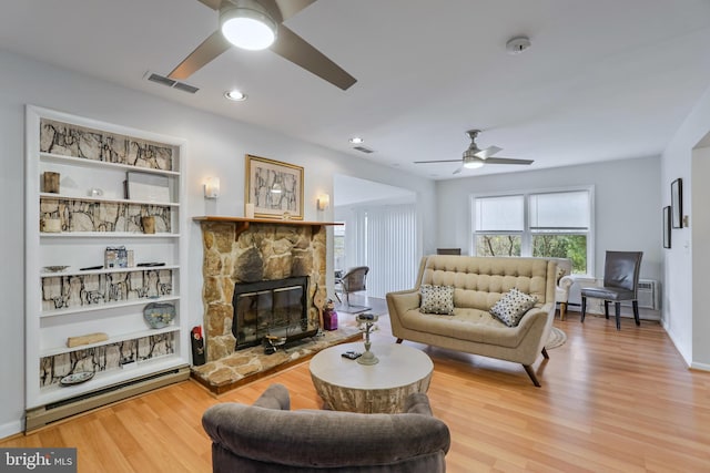 living room with light wood-type flooring, a stone fireplace, and ceiling fan