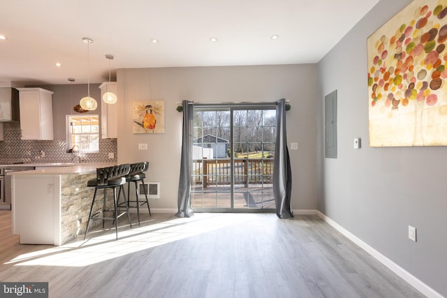 kitchen featuring light hardwood / wood-style floors, white cabinetry, a kitchen breakfast bar, decorative light fixtures, and backsplash