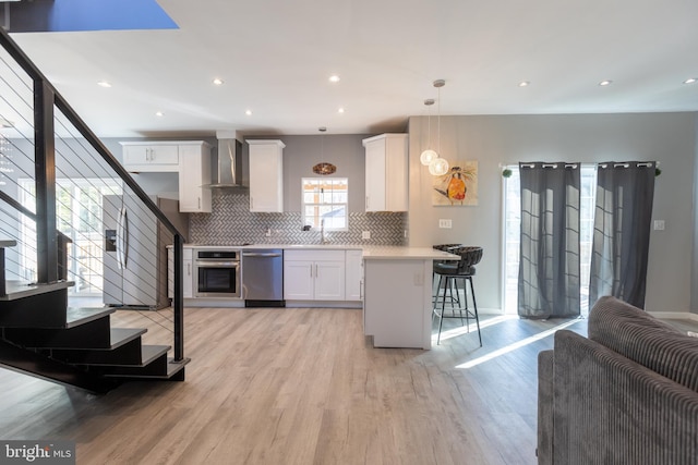 kitchen with stainless steel appliances, white cabinets, a kitchen breakfast bar, wall chimney range hood, and pendant lighting