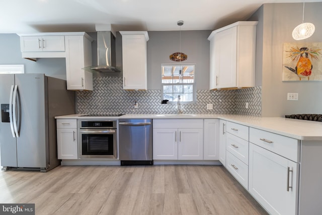 kitchen with stainless steel appliances, hanging light fixtures, sink, wall chimney range hood, and white cabinetry