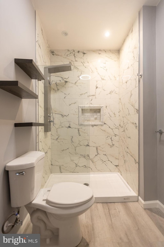 bathroom featuring a tile shower, wood-type flooring, and toilet