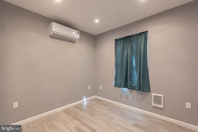 empty room featuring heating unit, light wood-type flooring, and a wall mounted air conditioner