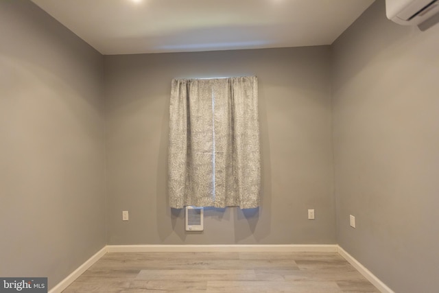 empty room with light wood-type flooring, heating unit, and a wall mounted AC