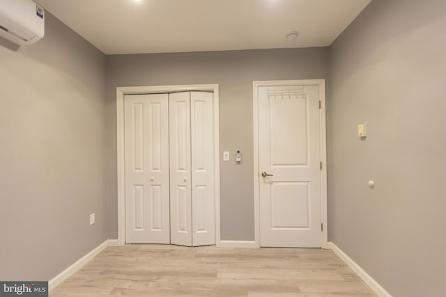 unfurnished bedroom with a wall unit AC and light hardwood / wood-style floors