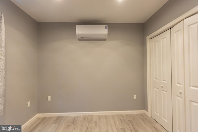 unfurnished bedroom featuring light wood-type flooring, an AC wall unit, and a closet