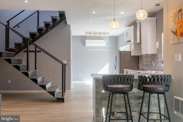 kitchen with white cabinets, light hardwood / wood-style flooring, hanging light fixtures, and a breakfast bar