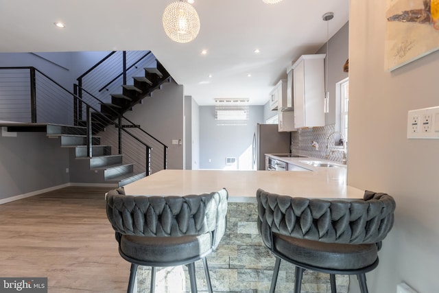 kitchen featuring tasteful backsplash, white cabinetry, pendant lighting, light hardwood / wood-style floors, and kitchen peninsula