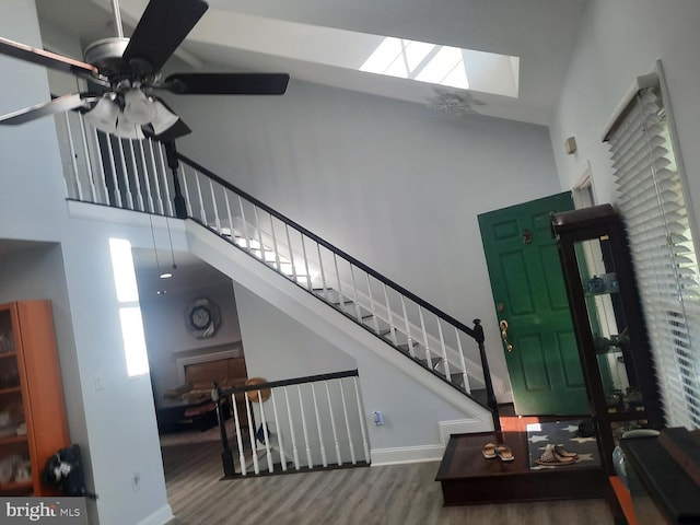 entryway featuring a skylight, hardwood / wood-style floors, ceiling fan, and a towering ceiling