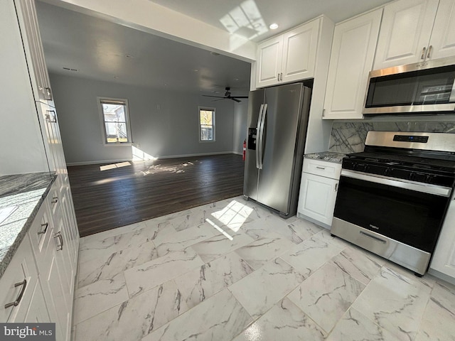 kitchen with white cabinetry, appliances with stainless steel finishes, ceiling fan, light wood-type flooring, and light stone counters