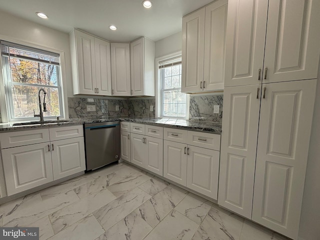 kitchen with stainless steel dishwasher, a sink, white cabinets, light marble finish floors, and dark stone counters