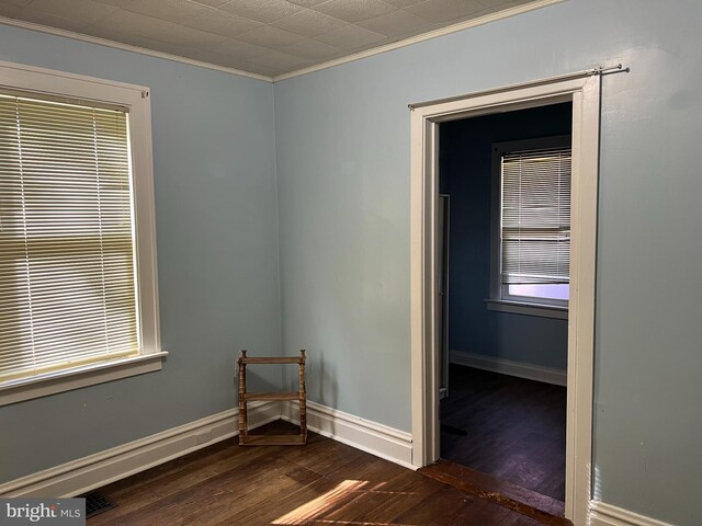 empty room featuring crown molding, baseboards, and dark wood-style flooring