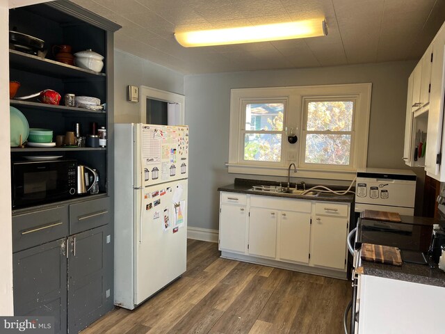 kitchen featuring dark countertops, black microwave, dark wood finished floors, freestanding refrigerator, and a sink