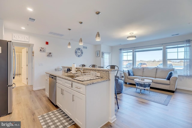 kitchen featuring a center island with sink, appliances with stainless steel finishes, light hardwood / wood-style floors, light stone counters, and white cabinetry