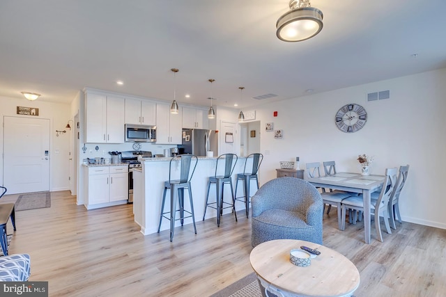 kitchen with a center island, white cabinets, hanging light fixtures, light stone counters, and stainless steel appliances