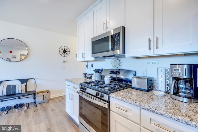 kitchen featuring light stone countertops, white cabinetry, light wood-type flooring, and appliances with stainless steel finishes