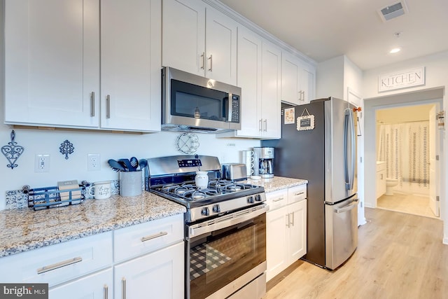 kitchen featuring white cabinets, stainless steel appliances, light hardwood / wood-style flooring, and light stone counters