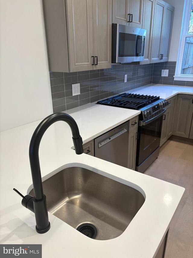 kitchen featuring backsplash, sink, stainless steel appliances, and light wood-type flooring