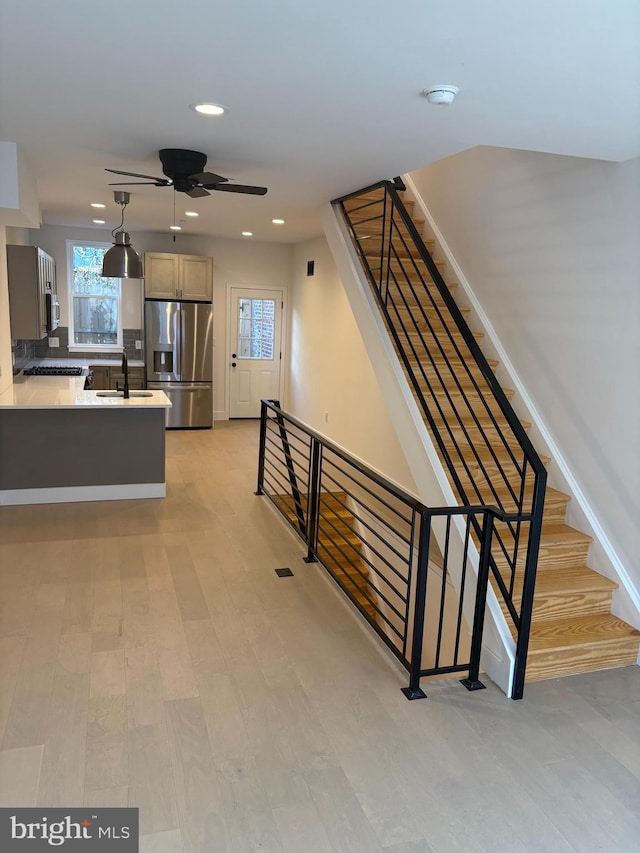 staircase with ceiling fan, wood-type flooring, and sink