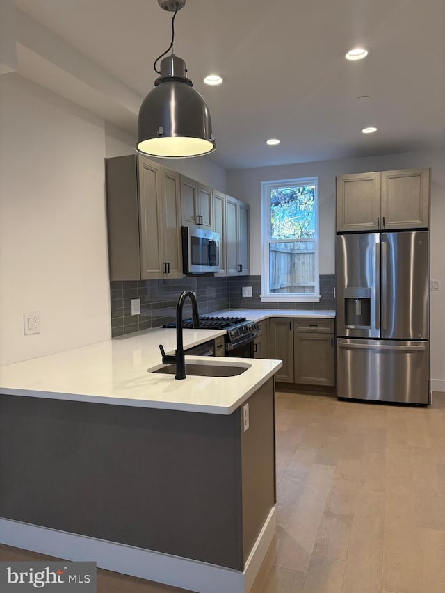 kitchen with pendant lighting, sink, light hardwood / wood-style floors, kitchen peninsula, and stainless steel appliances