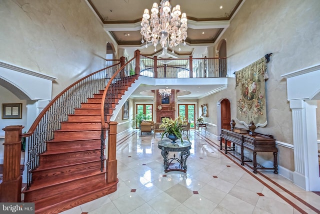 tiled foyer entrance with a high ceiling, decorative columns, crown molding, and a notable chandelier