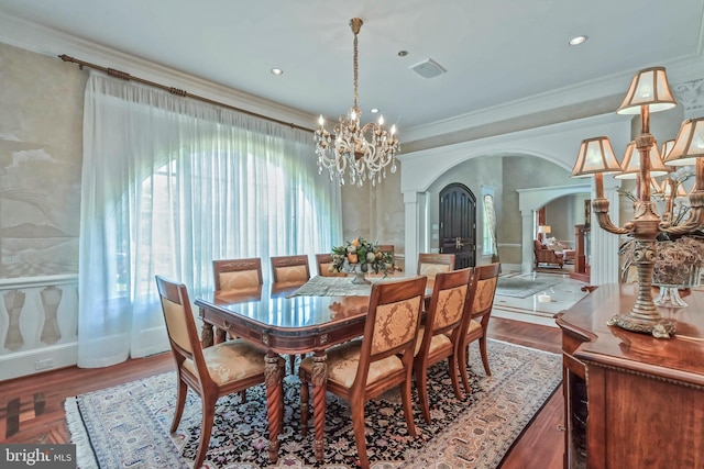 dining area with wood-type flooring, ornamental molding, ornate columns, and a chandelier