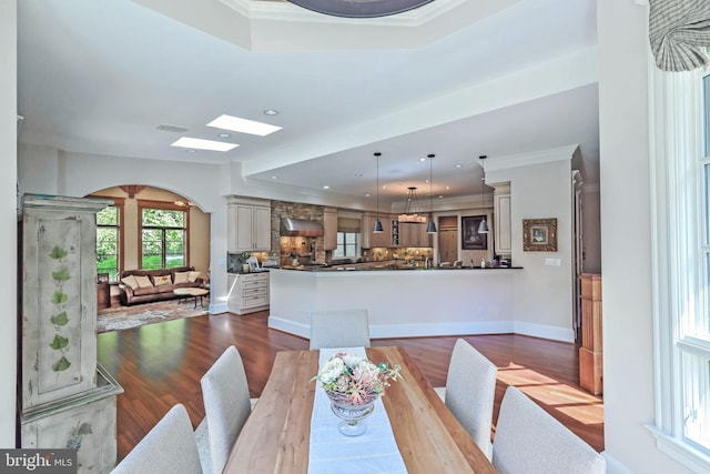 dining room featuring a tray ceiling, a skylight, dark hardwood / wood-style floors, and ornamental molding