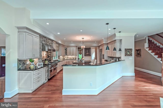 kitchen featuring decorative light fixtures, dark hardwood / wood-style flooring, range with two ovens, and wall chimney range hood