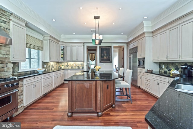 kitchen featuring crown molding, hanging light fixtures, built in appliances, dark hardwood / wood-style floors, and an island with sink