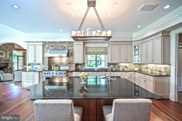 kitchen with high end range, dark wood-type flooring, wall chimney range hood, sink, and plenty of natural light