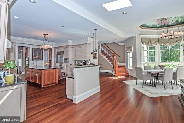 kitchen featuring hanging light fixtures, dark hardwood / wood-style flooring, stainless steel built in refrigerator, a kitchen island with sink, and ornamental molding