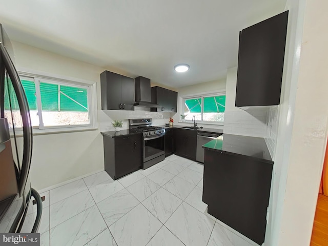 kitchen featuring wall chimney range hood, appliances with stainless steel finishes, sink, and backsplash