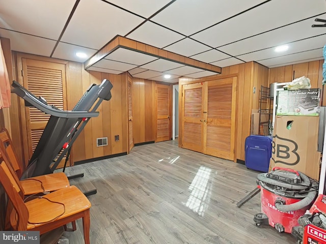 workout room featuring wood walls, light hardwood / wood-style floors, and a paneled ceiling