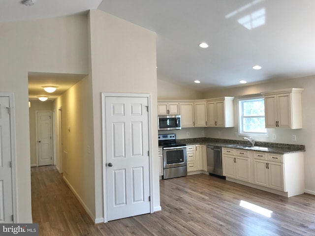 kitchen with stainless steel appliances, sink, cream cabinetry, light wood-type flooring, and vaulted ceiling