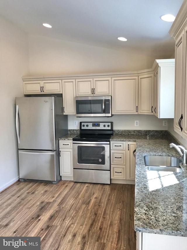 kitchen with sink, appliances with stainless steel finishes, dark stone counters, wood-type flooring, and vaulted ceiling