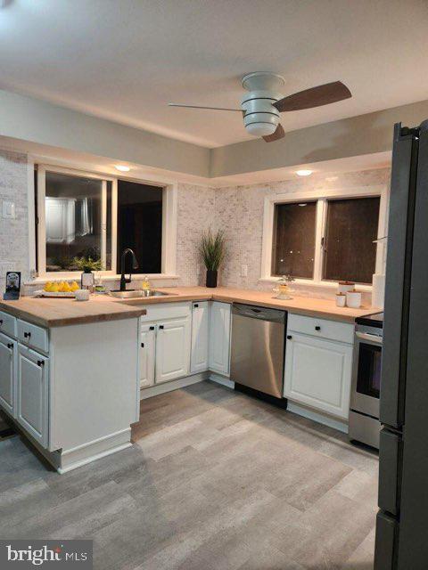 kitchen with white cabinets, sink, light hardwood / wood-style flooring, ceiling fan, and appliances with stainless steel finishes