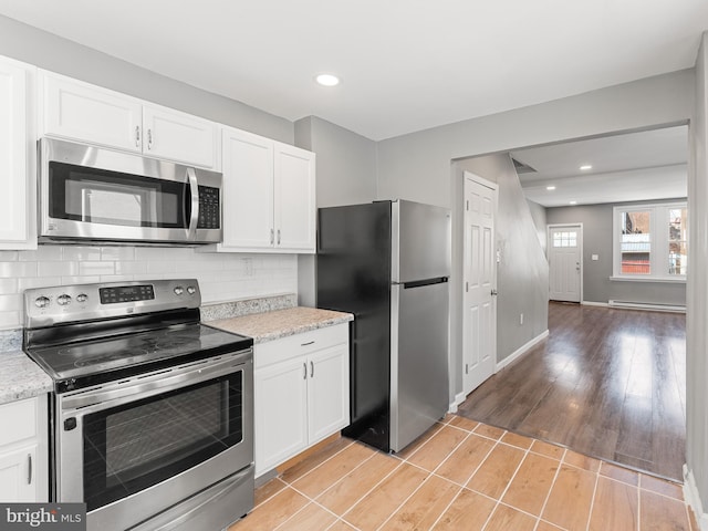 kitchen with a baseboard heating unit, stainless steel appliances, tasteful backsplash, white cabinetry, and light hardwood / wood-style flooring