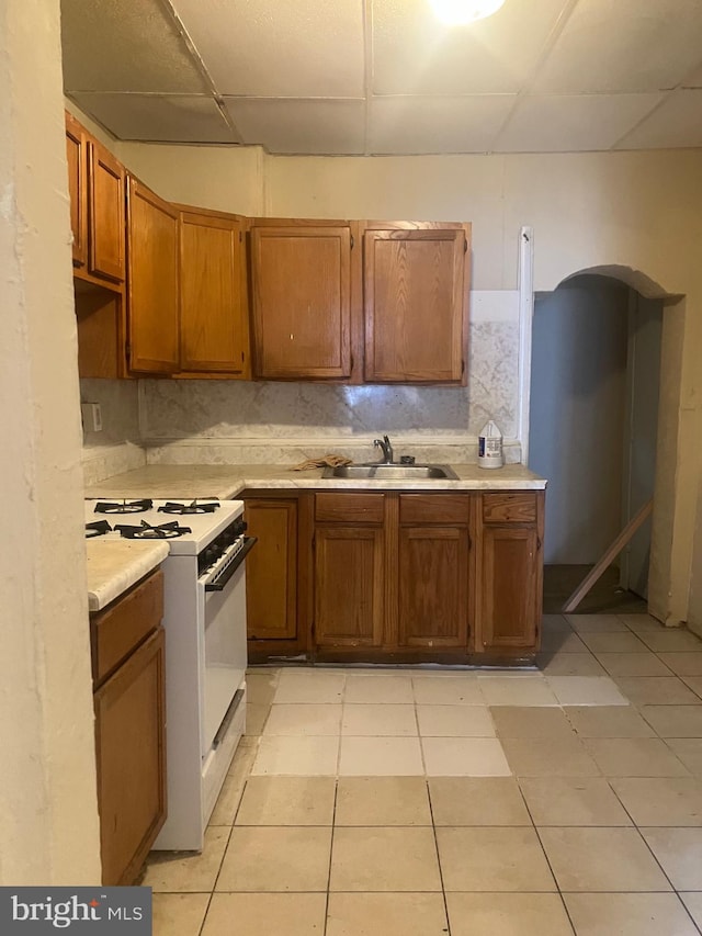 kitchen with a paneled ceiling, sink, light tile patterned floors, gas range gas stove, and backsplash